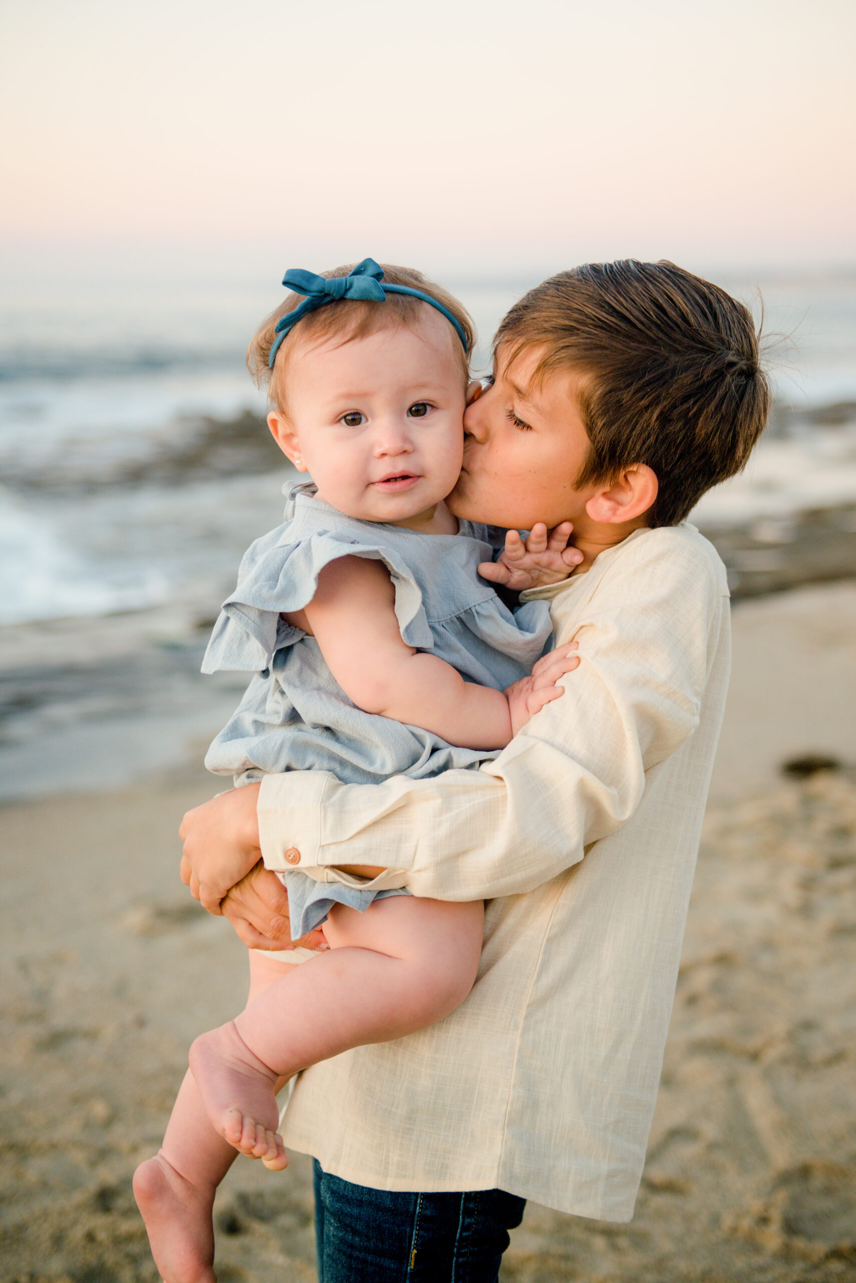 cute little boy holding his sister at the beach in san diego