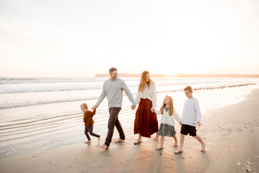 happy family holding hands and walking along the shoreline at the beach during sunset in coronado, california