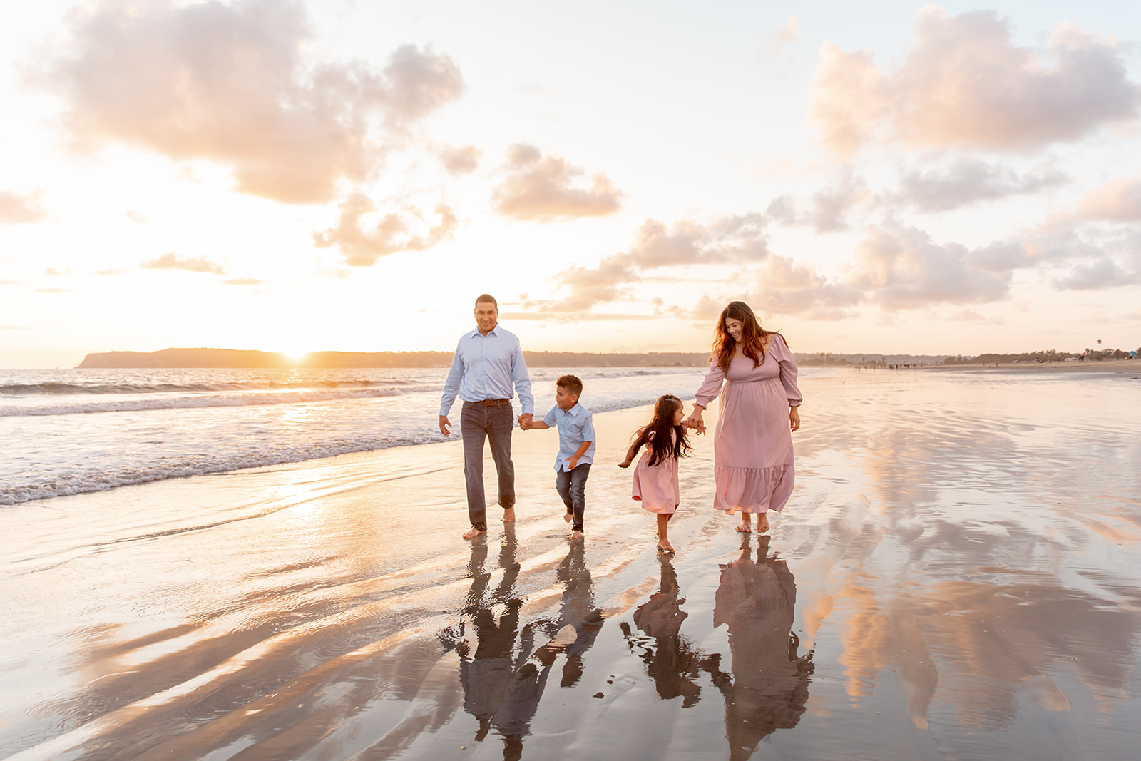 A mother and father walk down a wet beach holding hands with their young son and daughter in matching outfits on one of the Best san diego beaches for families