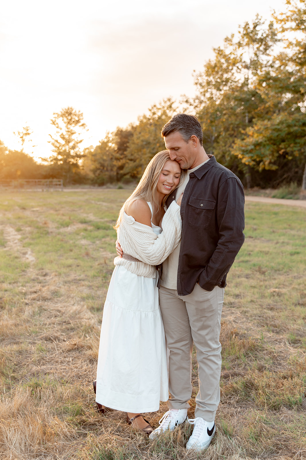 A couple stands in a grass field at sunset as she leans onto his chest San Diego Family Restaurants