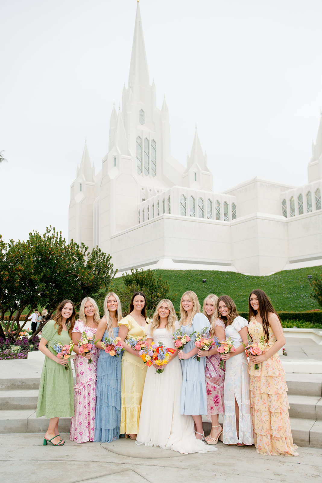 A bride stands with her colorful bridal party in a park before a Twin Oaks House Weddings