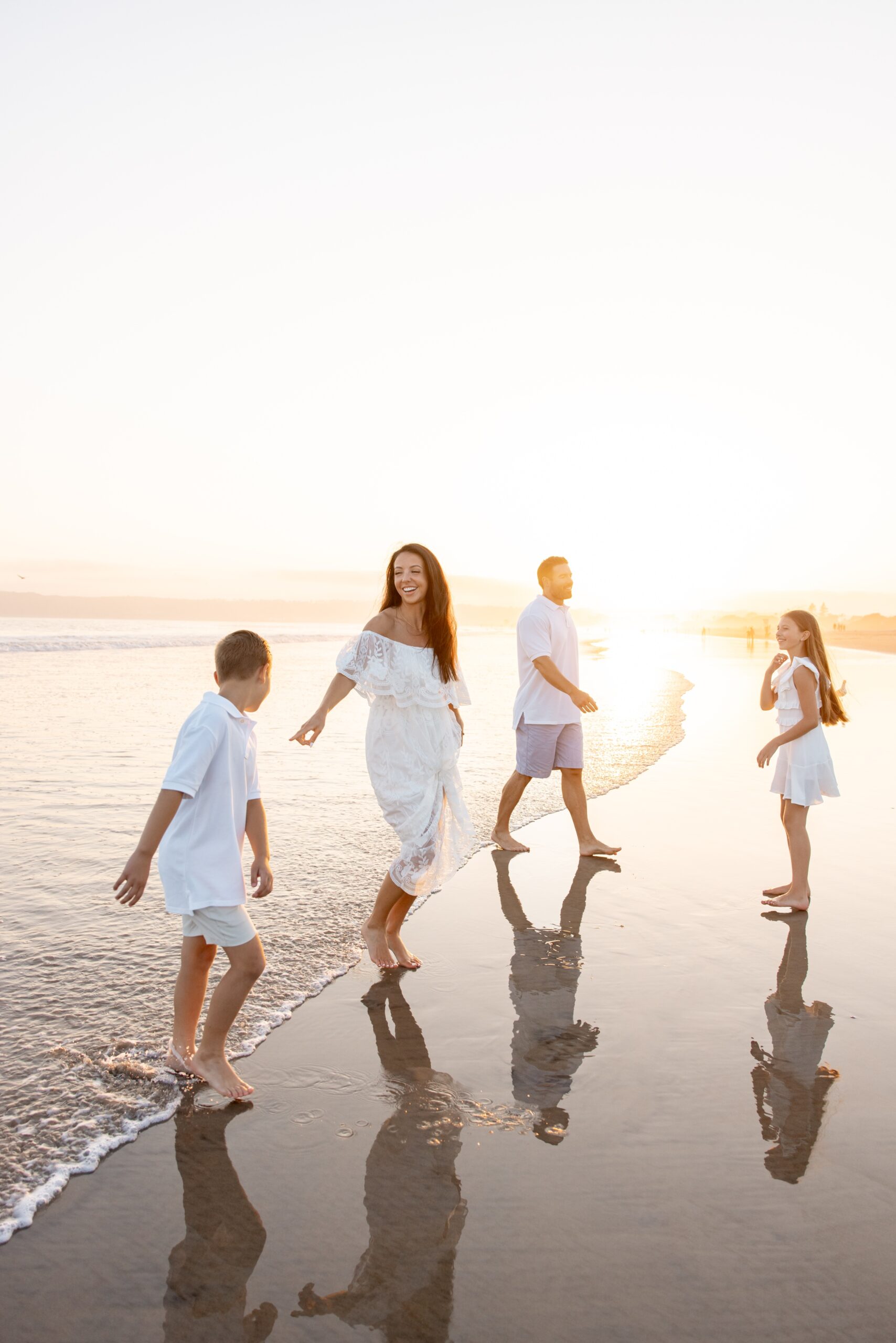 A mom and dad laugh and play with their young daughter and son on a beach at sunset