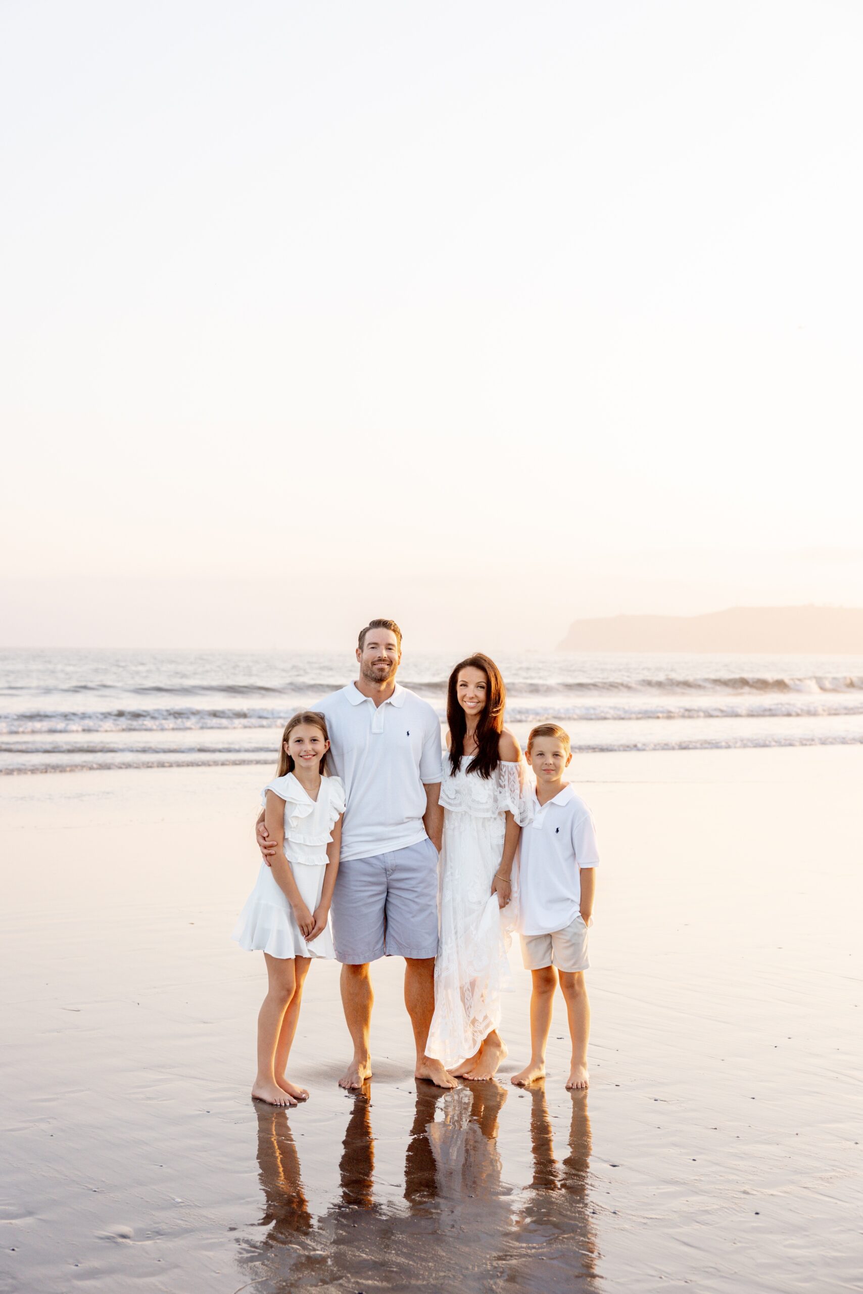 A mom and dad smile on a beach hugging their young son and daughter at sunset after some horseback riding lessons for kids san diego