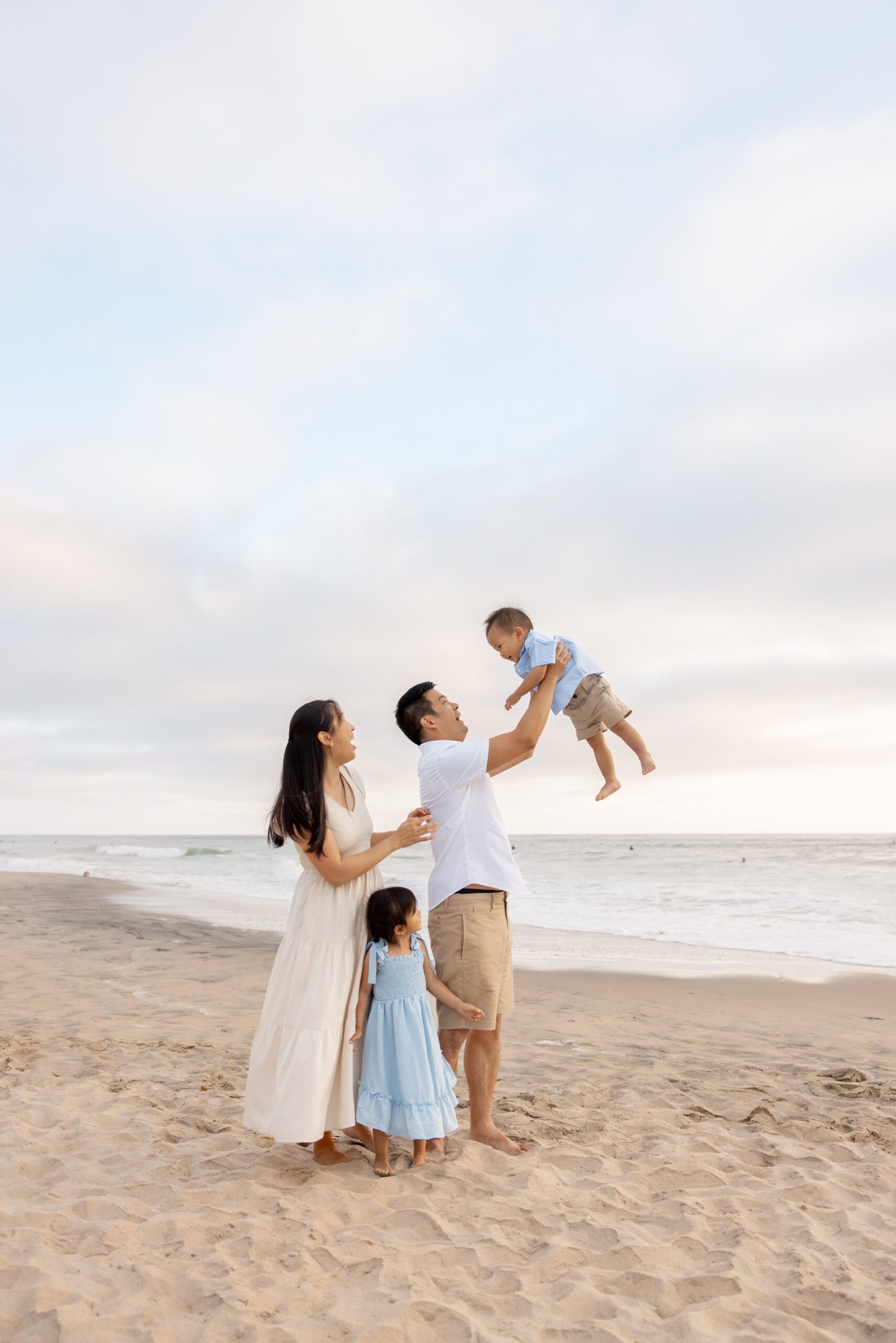 A happy family plays on a beach with two toddlers in blue after finding montessori daycare in san diego