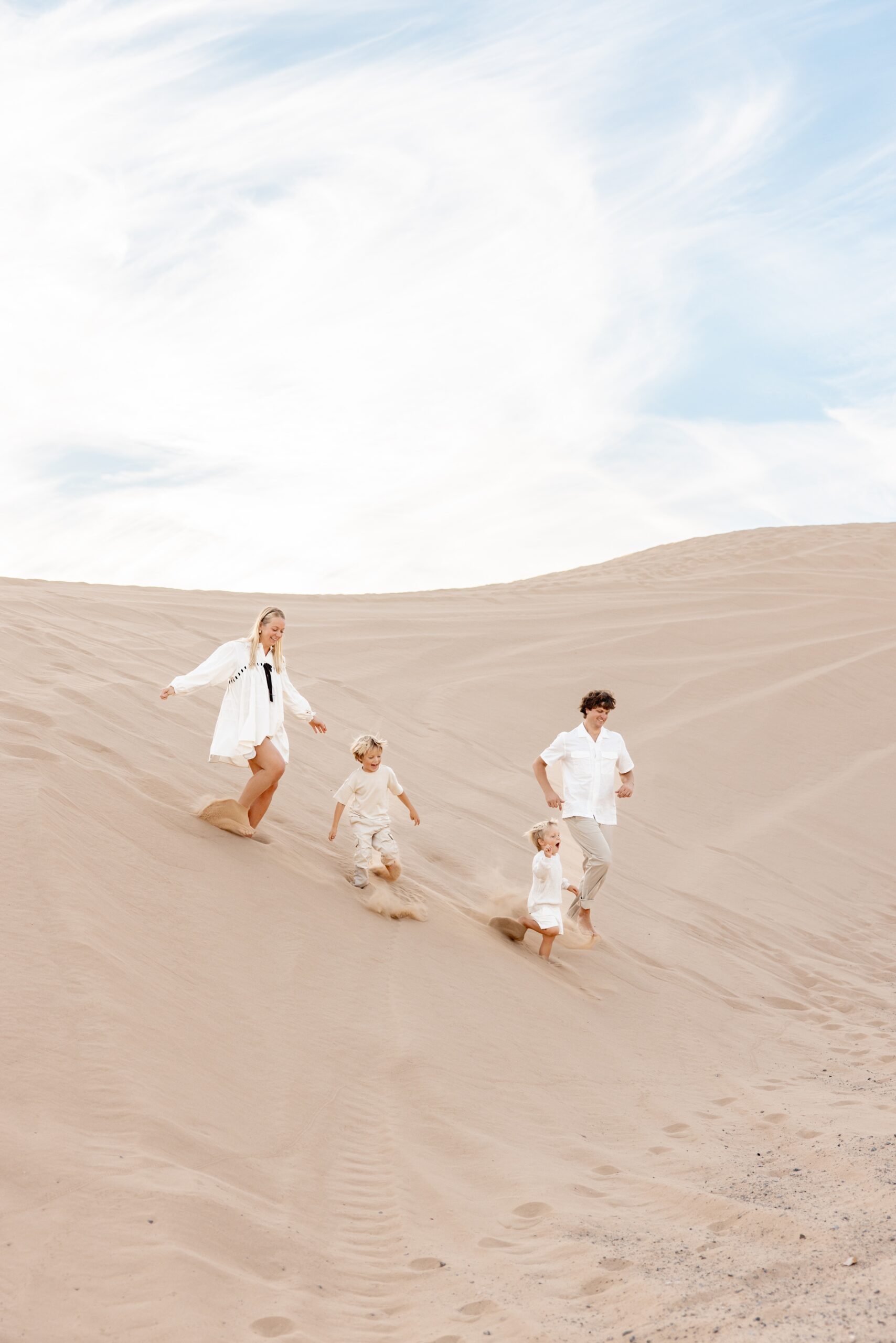 A family of 4 laugh while running down a large sand dune after visiting montessori schools in san diego