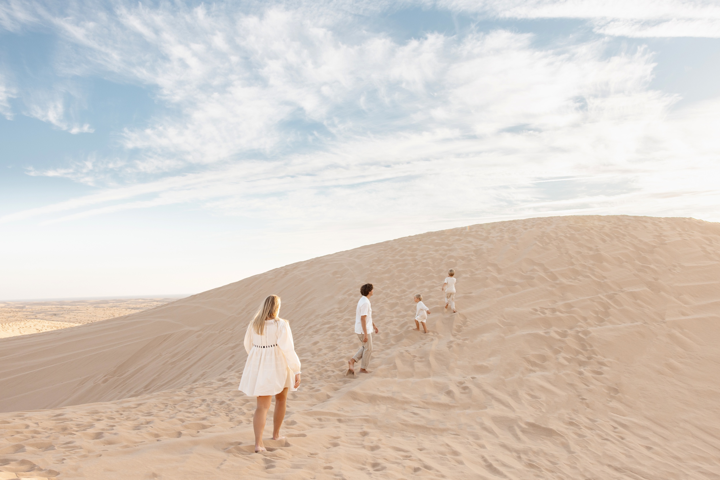 Two young children lead their parents up sand dunes at sunset in white after visiting montessori schools in san diego