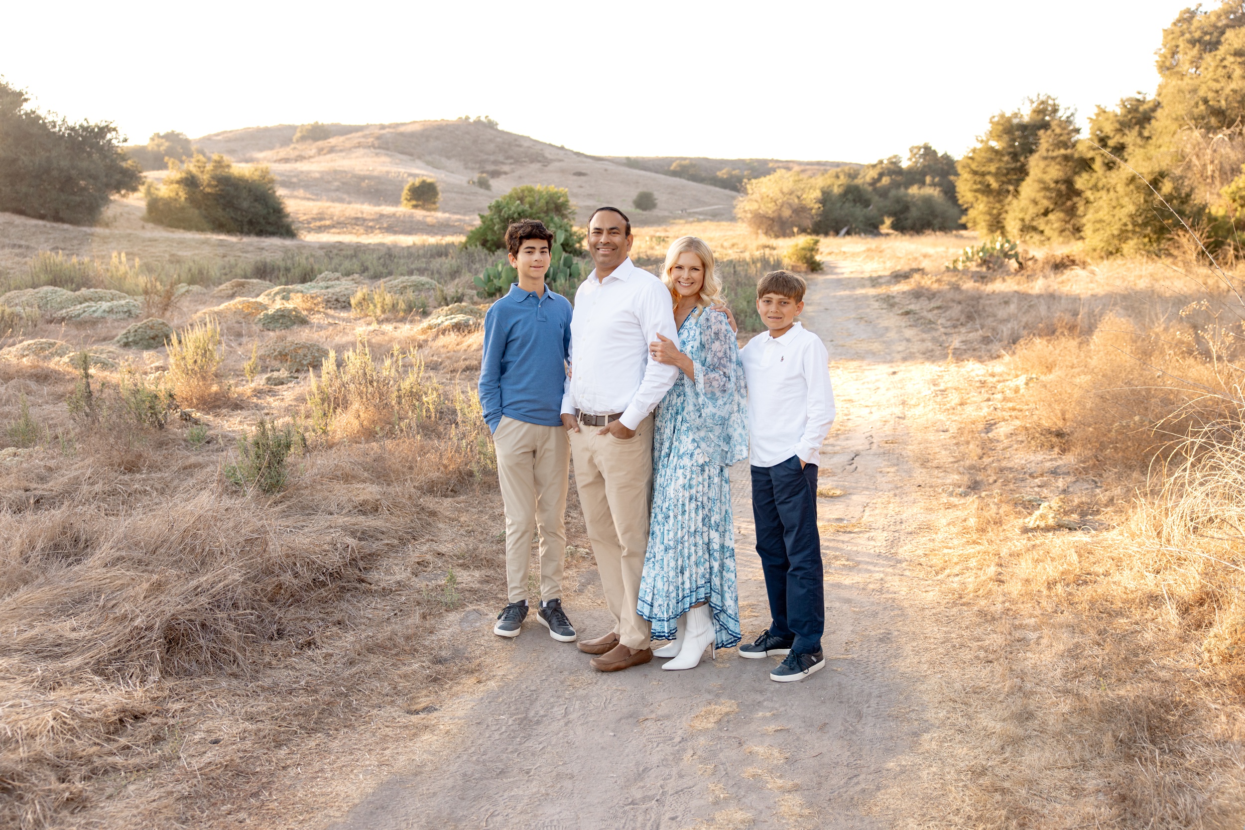 A happy family of four stand in a park trail at sunset smiling while attending private schools in san diego