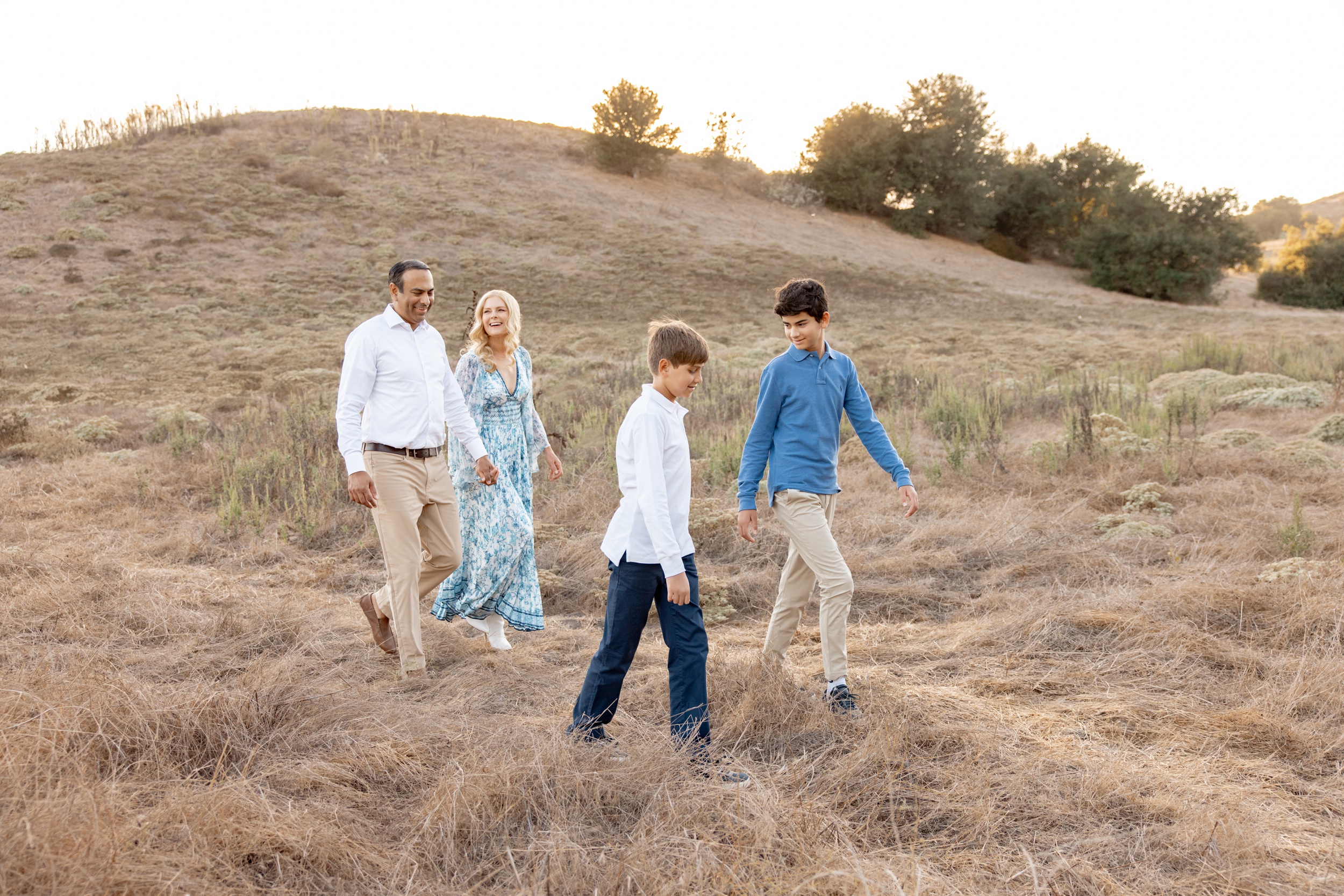 Two teen brothers walk through hills of tall gold grass with mom and dad behind them while attending private schools in san diego