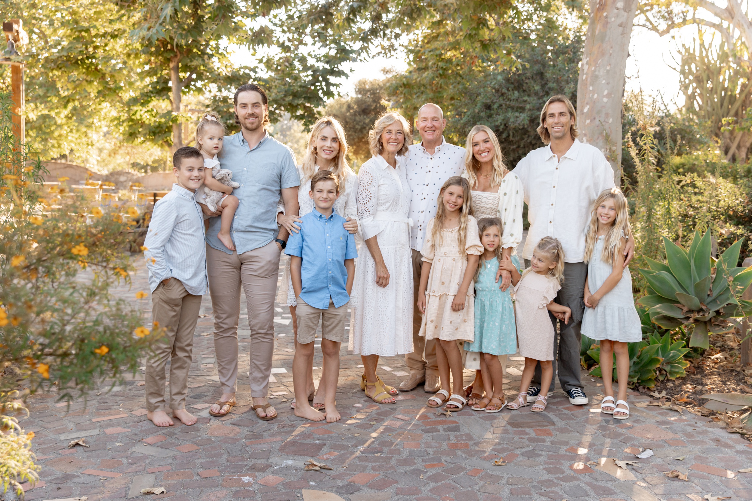 A large extended family stands in a garden patio at sunset smiling and hugging