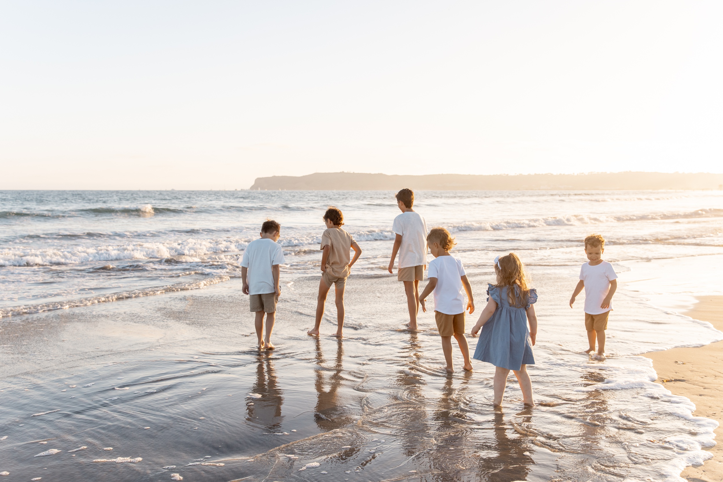 6 young siblings walk in the water at the beach at sunset while staying at best family resorts in san diego