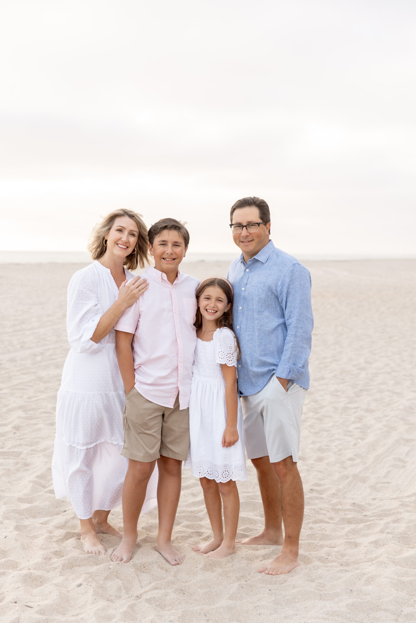 Happy mom and dad stand on a beach smiling with their young son and daughter while staying at best family resorts in san diego