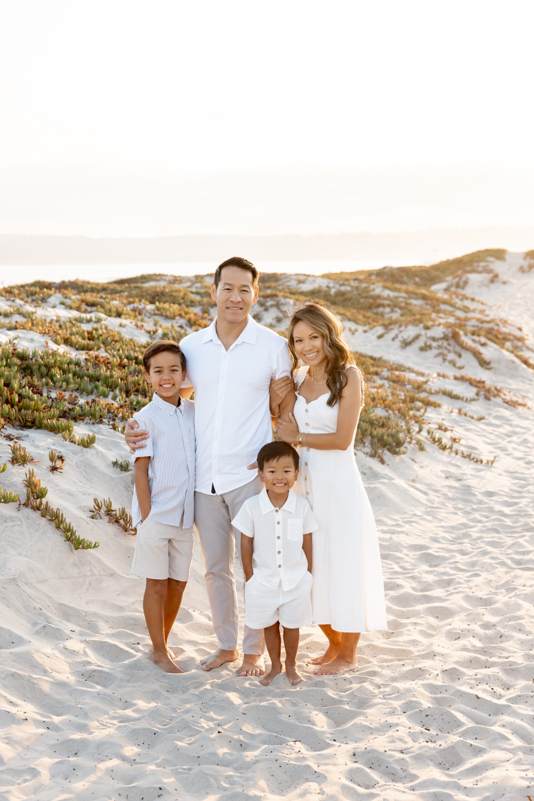 A happy family in all white hugs and smiles on a beach at sunset while staying at best luxury hotels in san diego for families