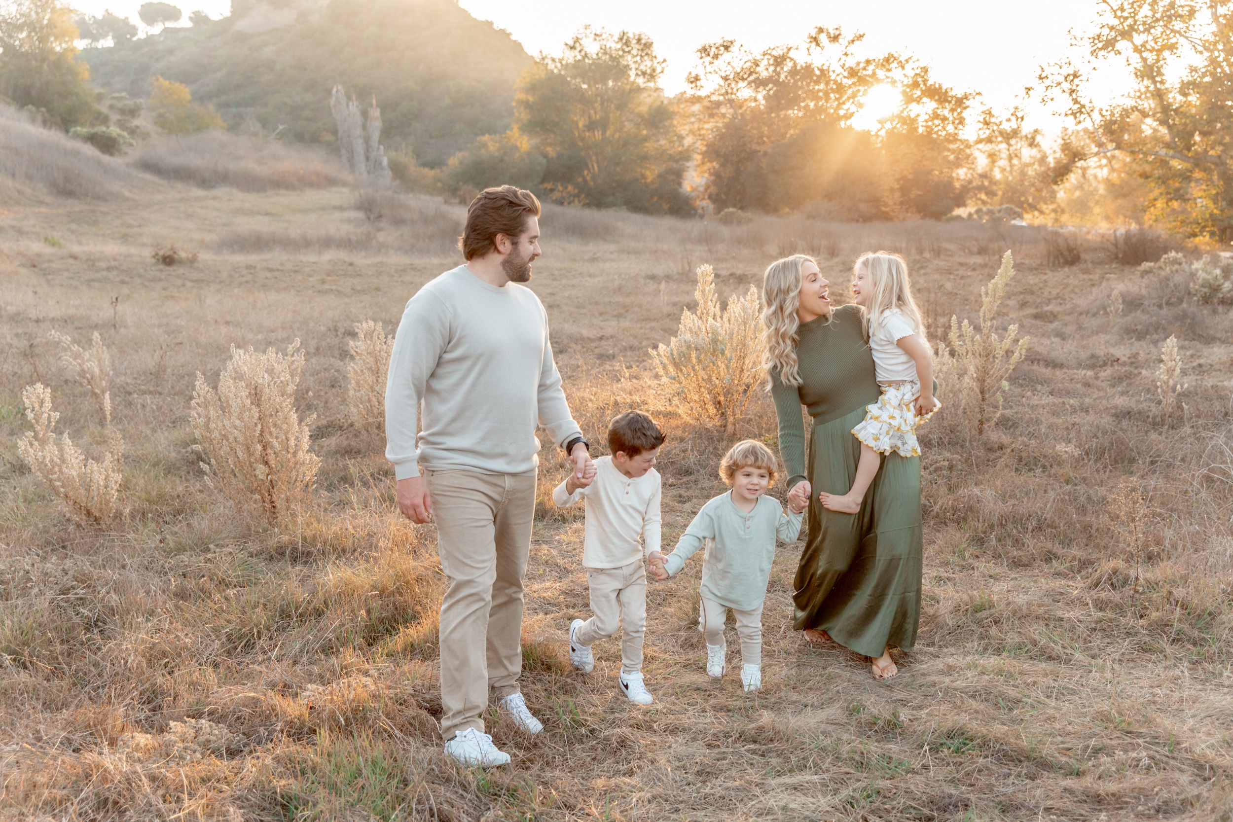 A happy family of 5 with 3 toddlers explore a trail at sunset holding hands and laughing