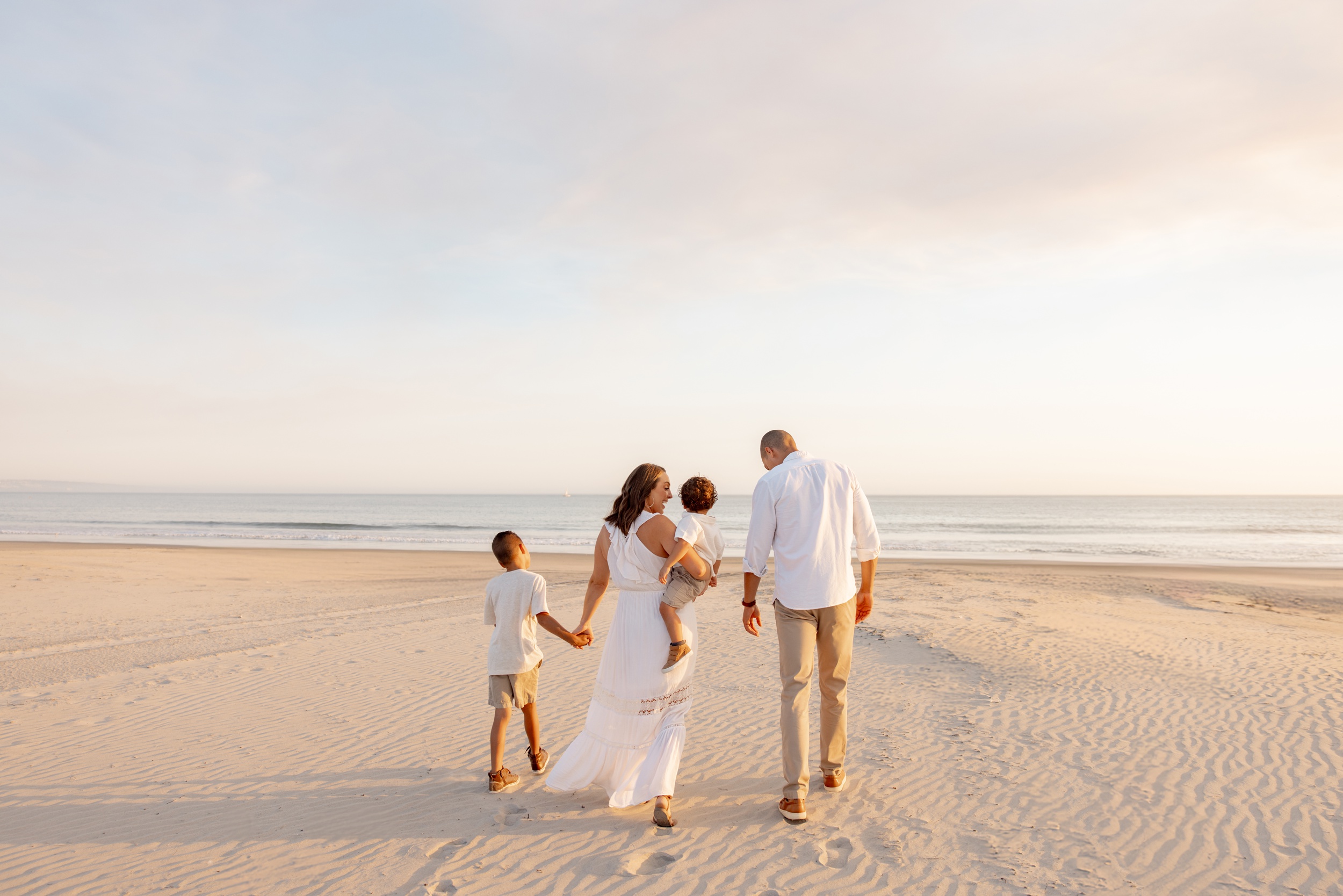 A happy family walks down a beach holding hands at sunset in white