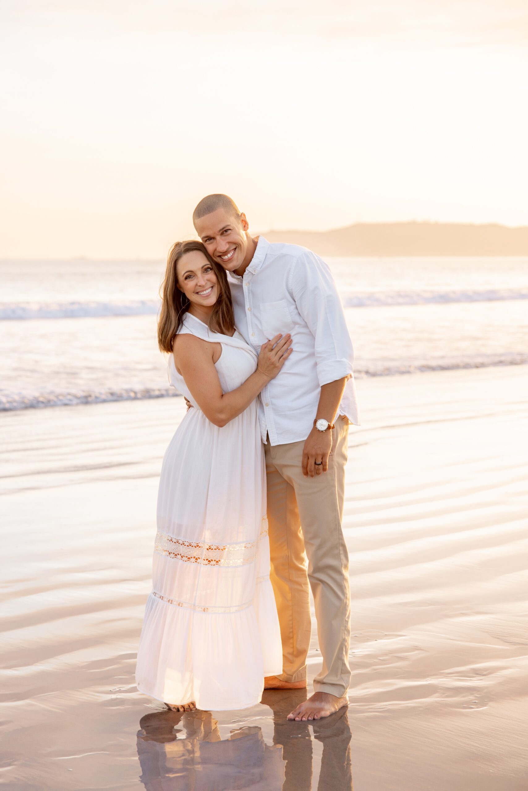 Happy mom and dad snuggle on a beach at sunset after some parenting classes in san diego