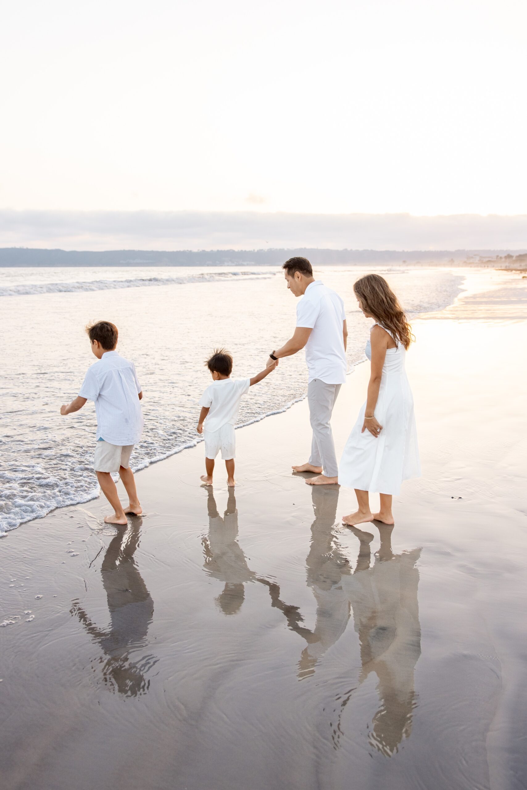 A happy family in white at sunset playing in the water on a beach before finding splash pads in san diego