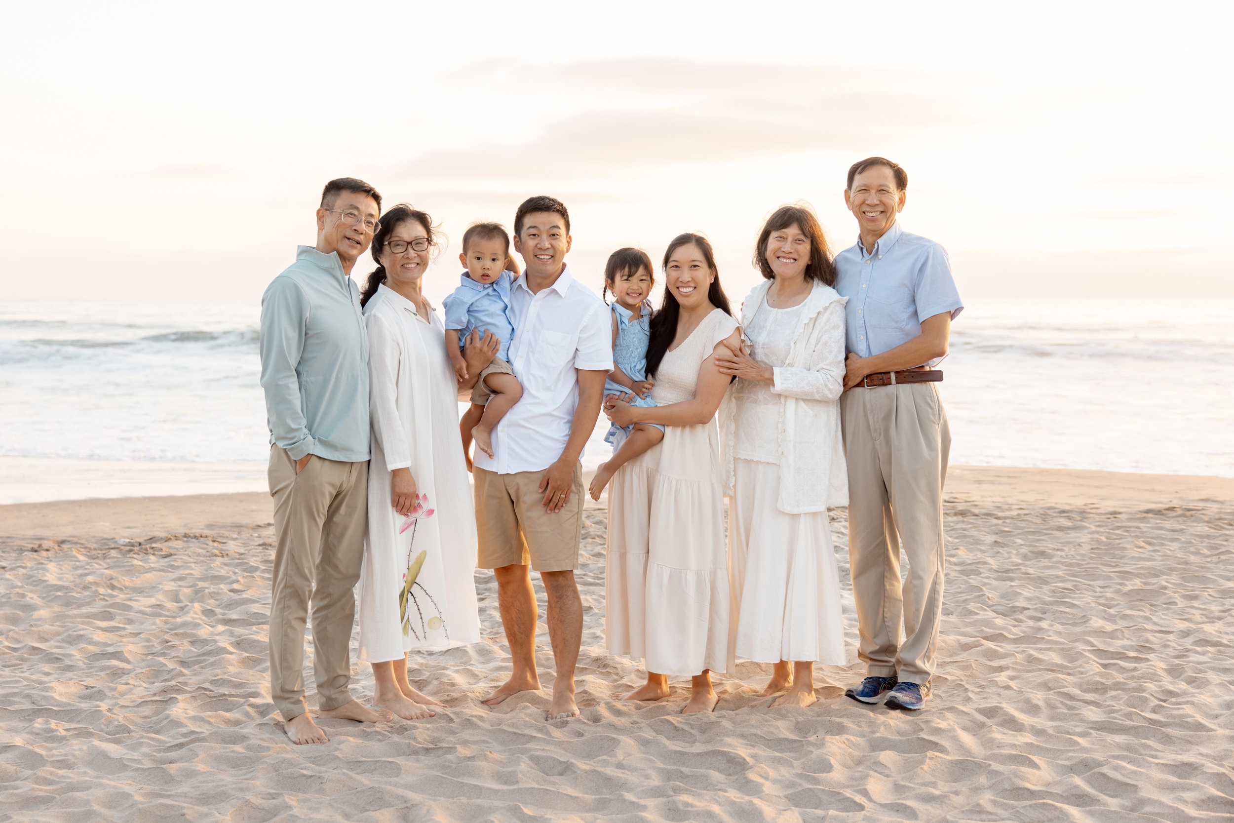 A happy extended family stands smiling together on a beach at sunset after finding stem summer camps in san diego