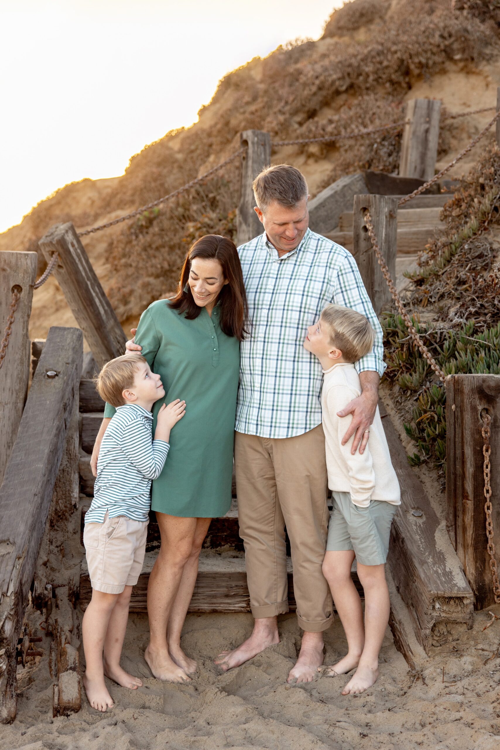 Young boys smile up to mom and dad while hugging on a beach access steps after finding tutors in san diego