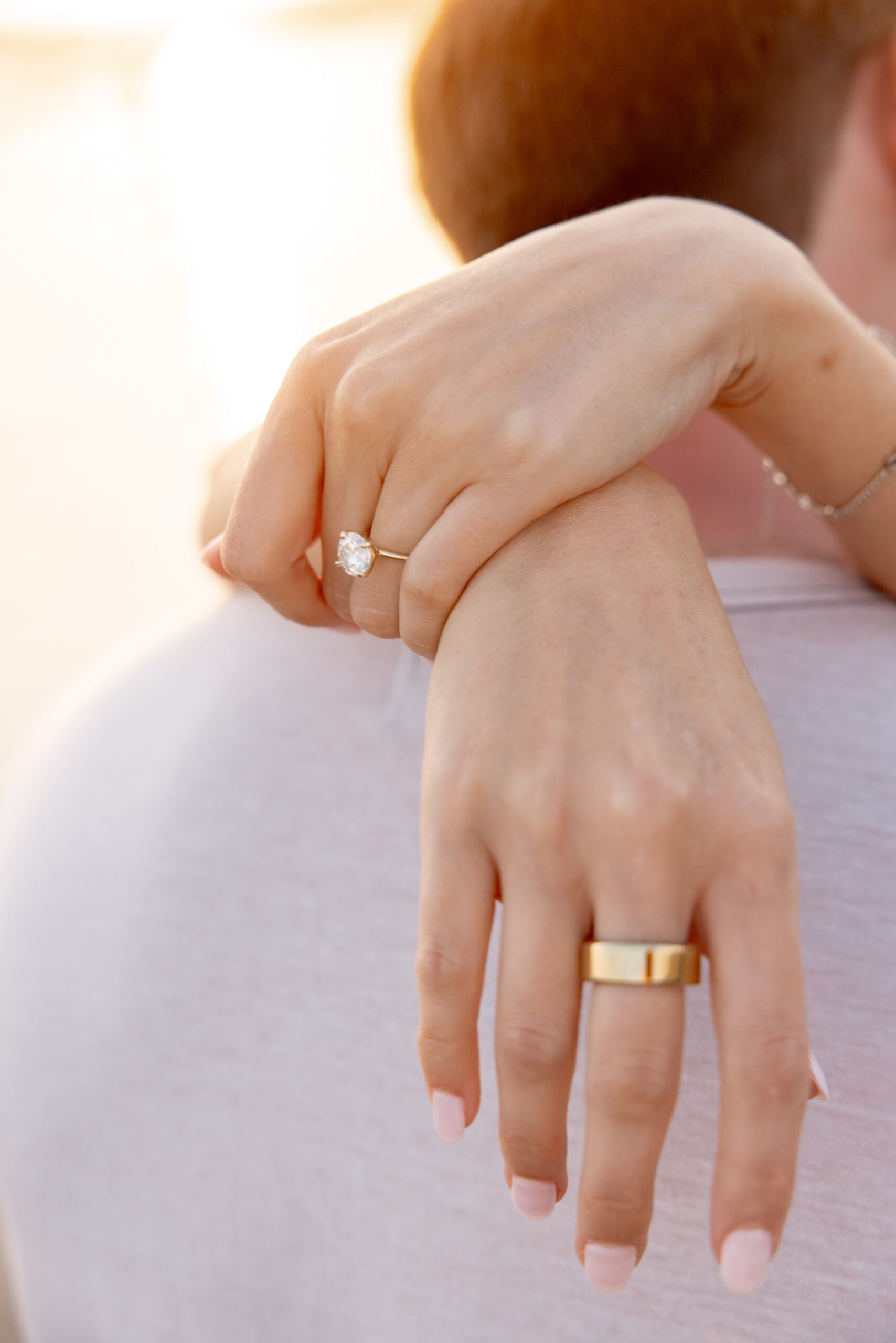 Details of an engagement ring on a woman's finger while hugging her fiancee