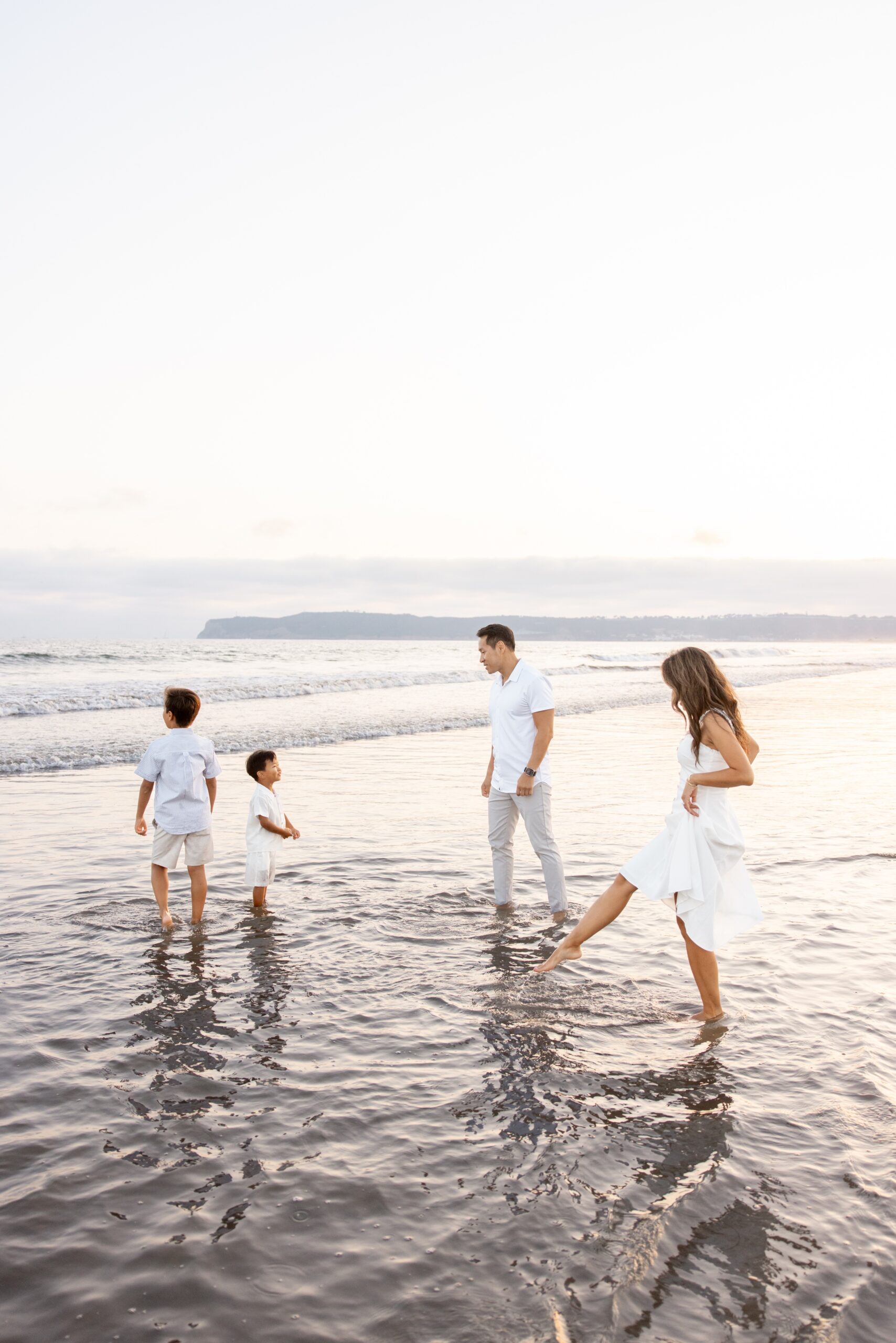 A mom and dad splash in the water with their two toddler sons in white outfits during fun things to do in San Diego with kids