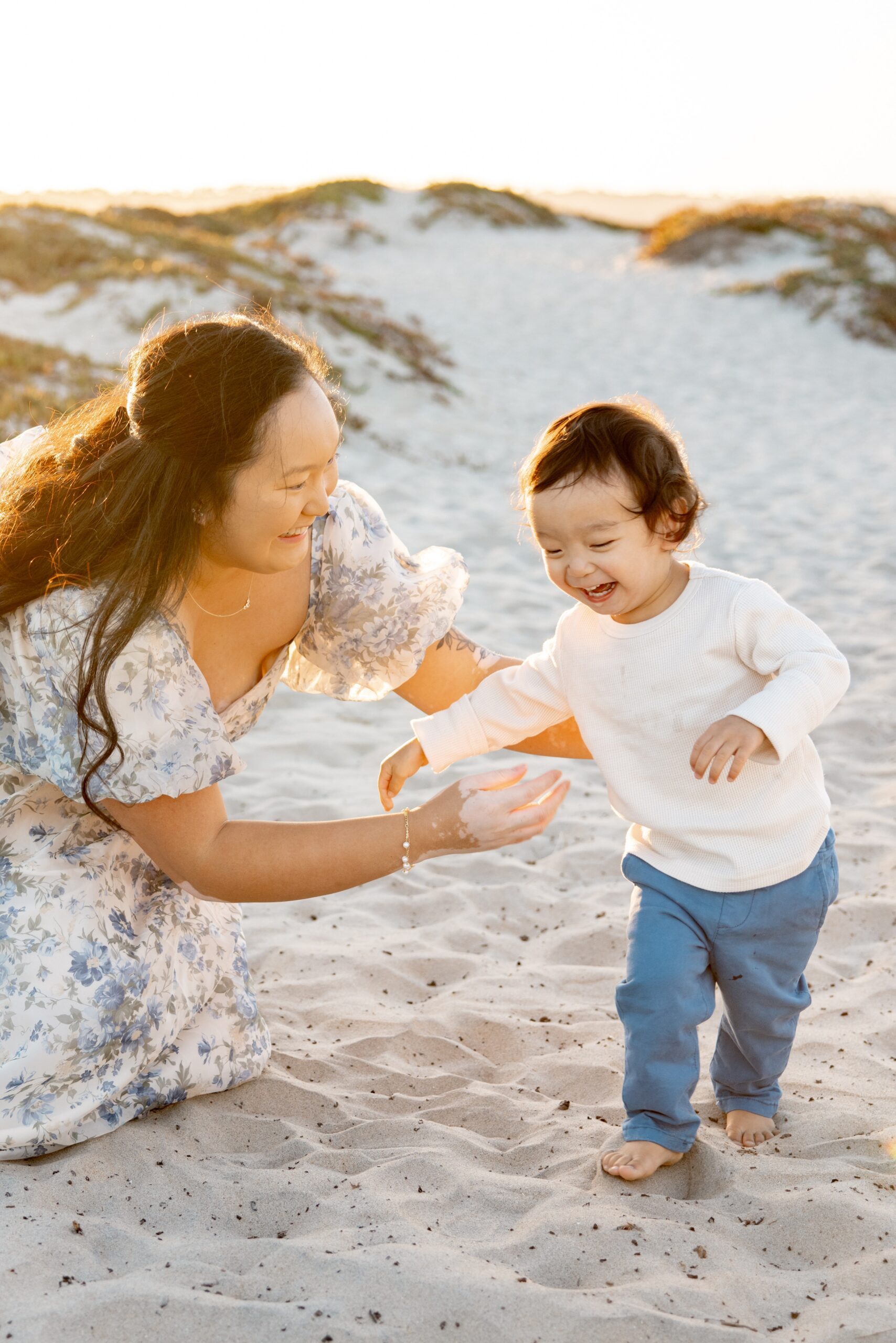 A giggling toddler plays with mom on a beach at sunset before visiting toddler-friendly restaurants in San Diego