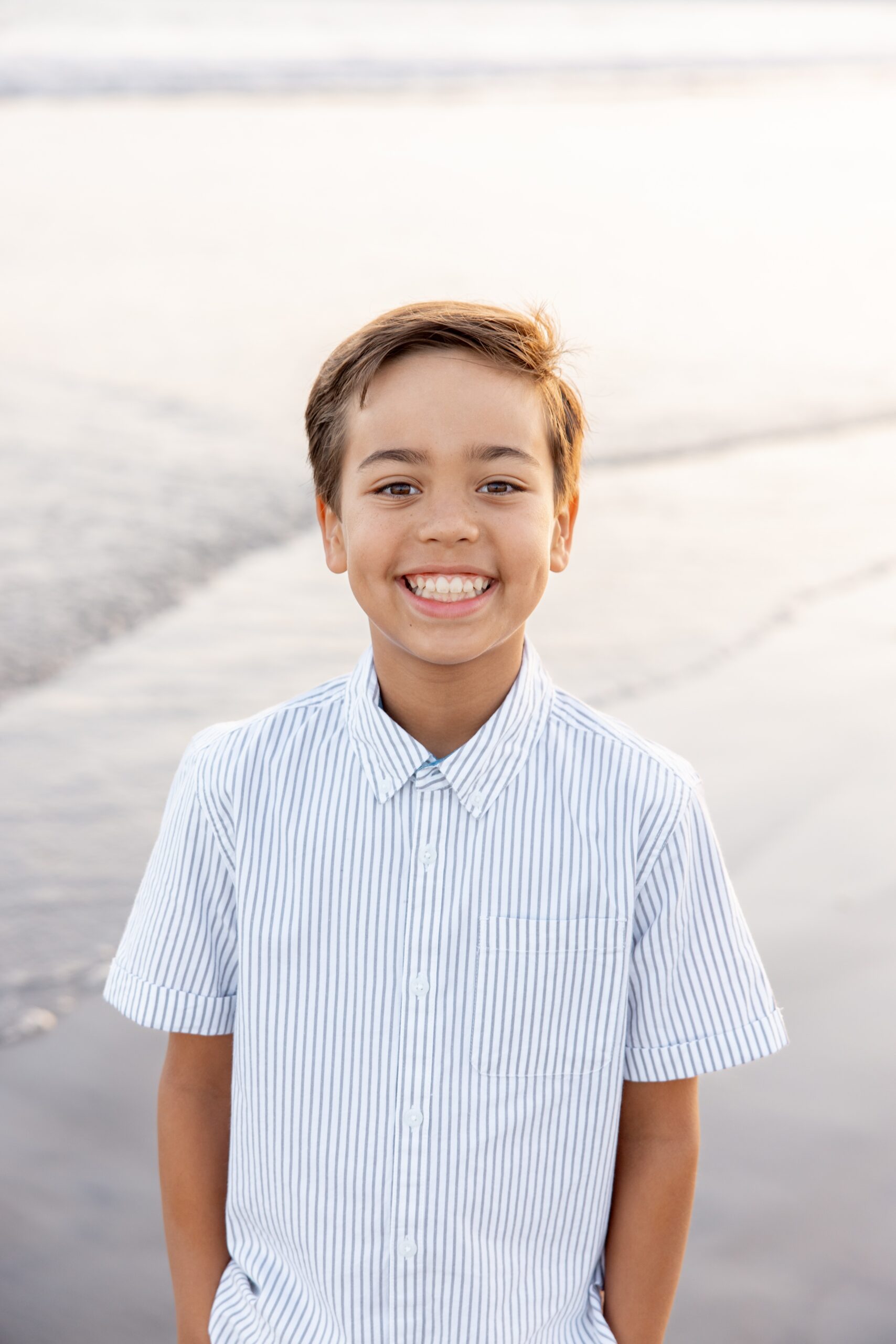 A happy young boy in a white stripe shirt smiles on a beach with hands in pockets before visiting the san diego zoo with kids