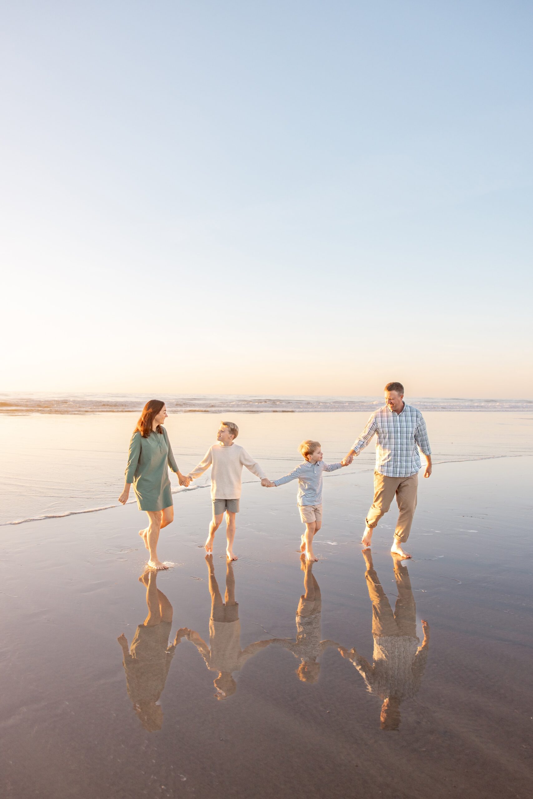 A happy family of 4 walk hand in hand on a beach at sunset