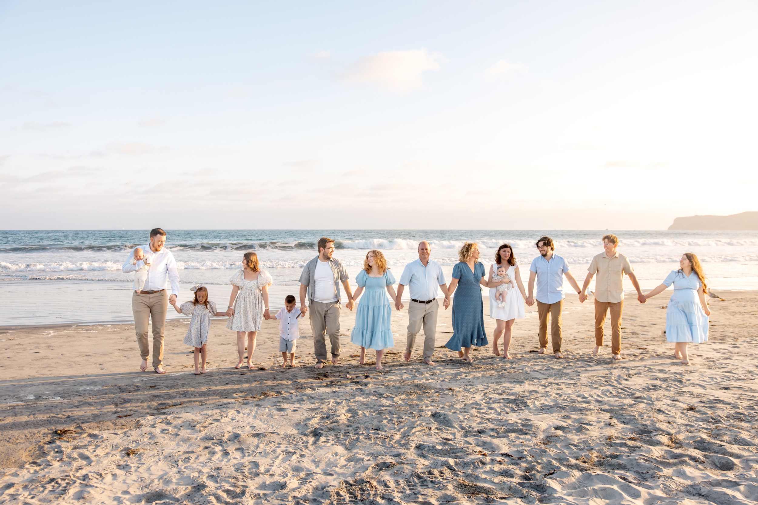 A large extended family of three generations walk on a beach holding hands and laughing before watching Big Bay Boom
