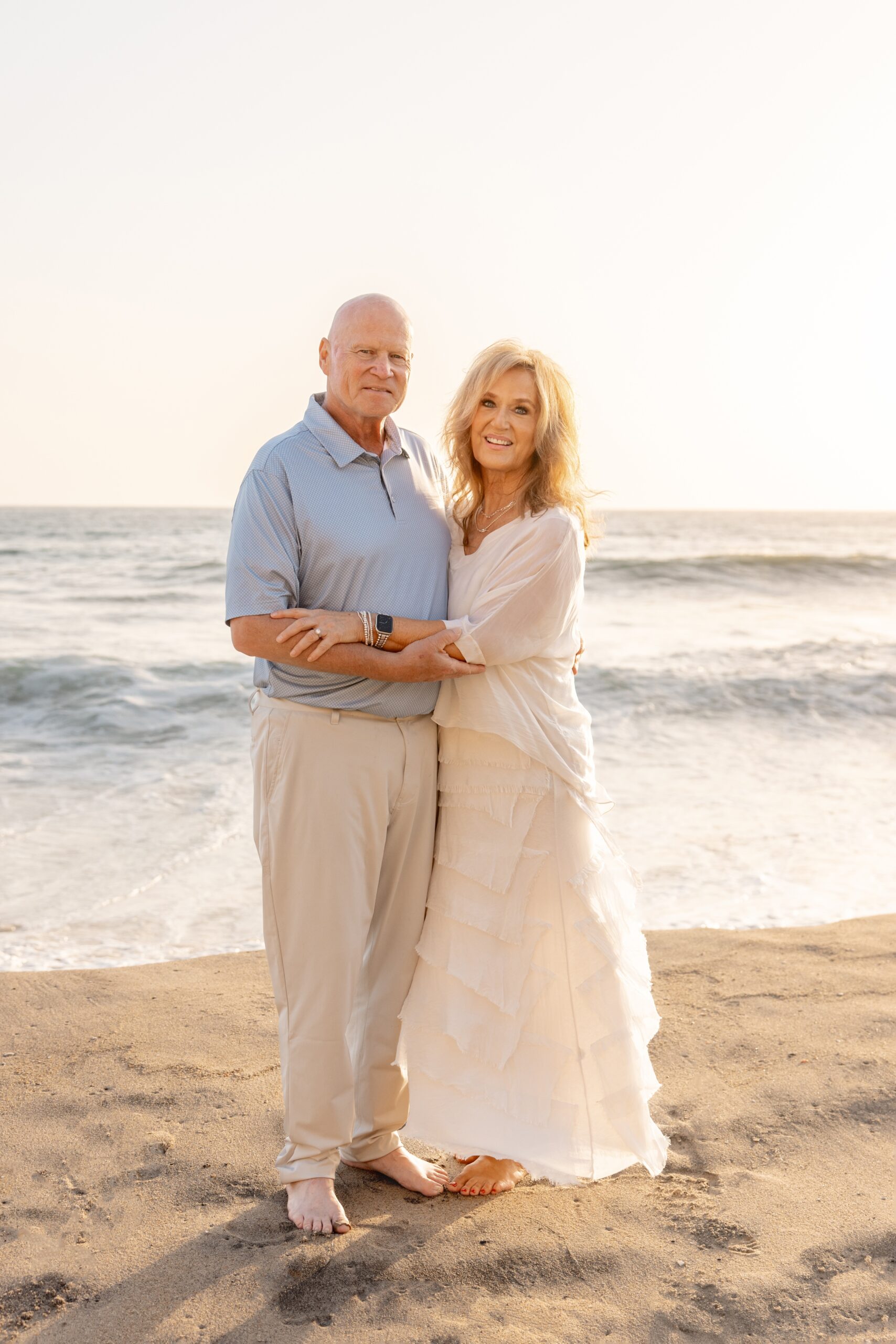 Smiling grandma and grandpa snuggle and hug on a beach at sunset