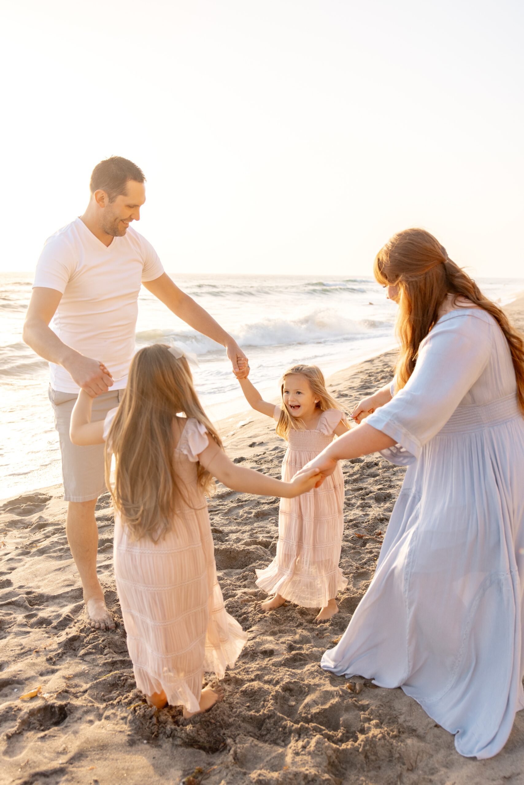 Happy toddler girls dance in a circle holding hands with mom and dad on a beach after riding a hot air balloon in san diego