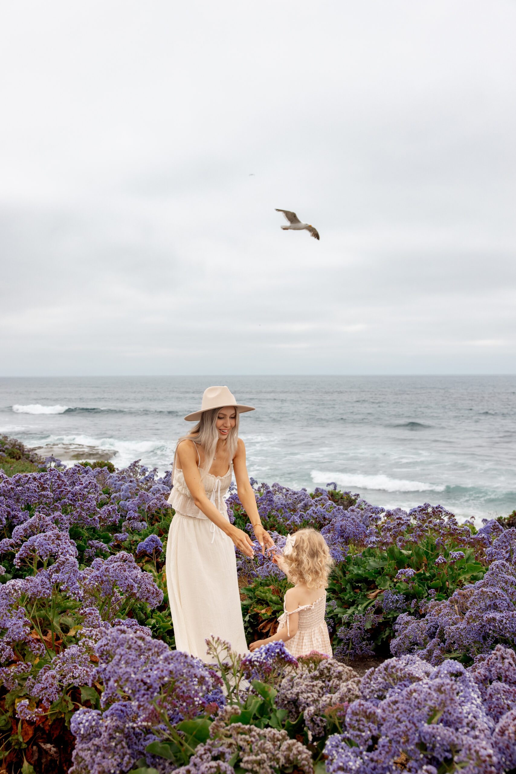 A happy mom explores purple wildflowers on the beach at sunset before visiting san diego restaurant week
