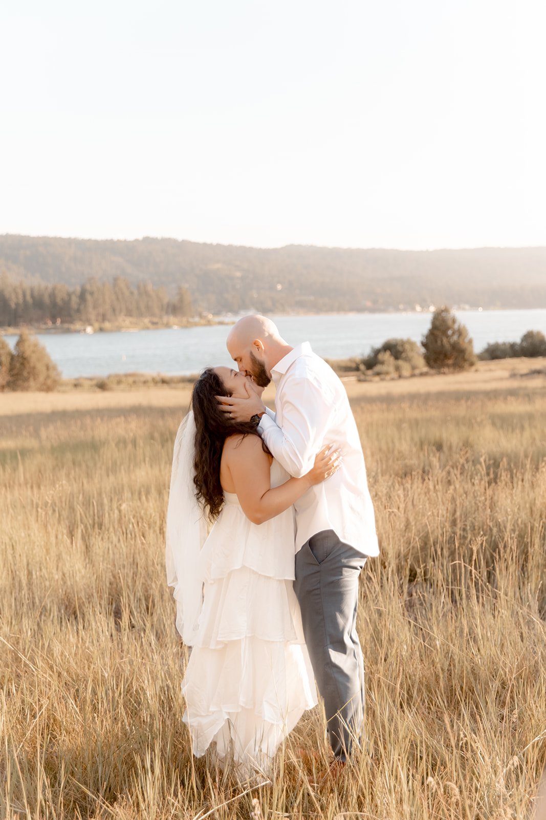 Newlyweds kiss in a field of tall golden grass overlooking a lake